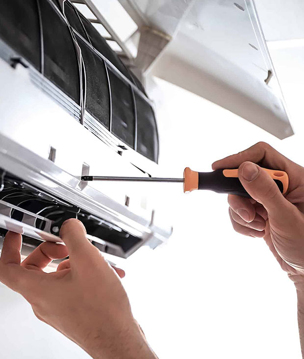 A man, representing Antrim Plumbing, fixes an air conditioner in the Philadelphia area using a screwdriver for effective air conditioning repair services.