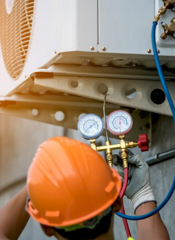 A man in a hard hat is working on an air conditioner for Antrim Plumbing.