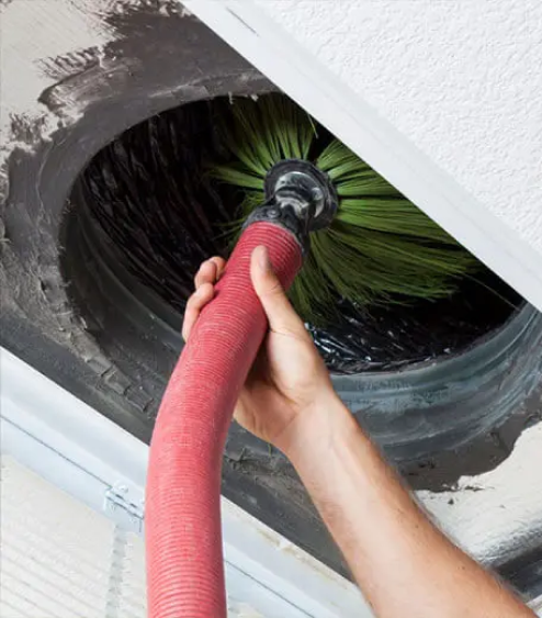 Antrim Plumbing offers air duct cleaning services by a professional man using a red hose to ensure healthy indoor air for your family.